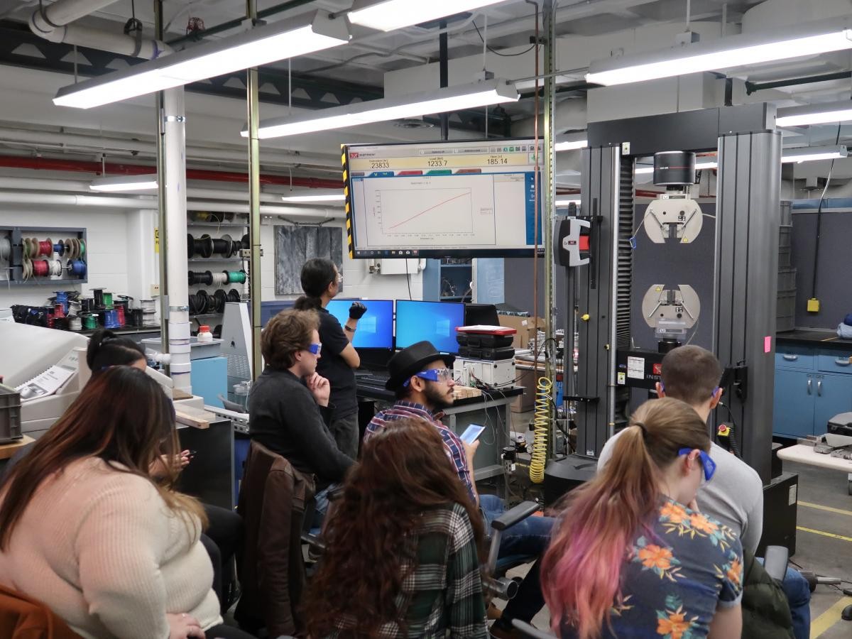 Students attending a lecture and demonstration about the density and strength of various types of wood using a 3-point bending test. Students attending CIEN 4300 class
